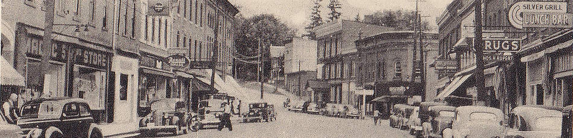 Postcard view of Madoc, Ontario, with 1930s cars parked on the side of the road.