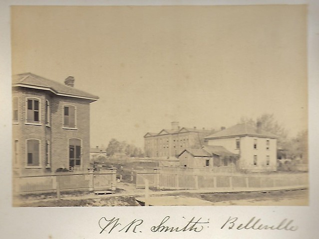 Old photograph of two houses and an institutional building in the background.