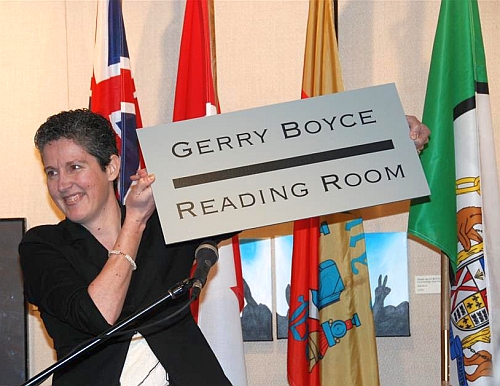Amanda Hill with a sign naming the Gerry Boyce Reading Room.