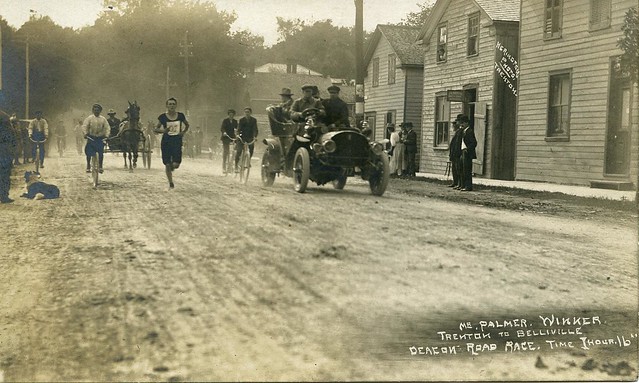 Man running in a road race with a car alongside him.