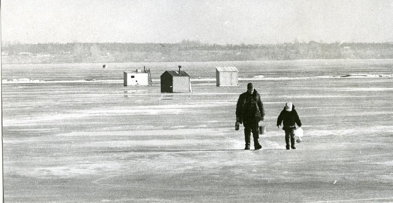 Man and child walking away from ice-fishing huts on frozen Bay of Quinte.