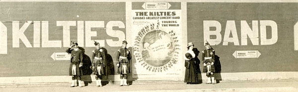 Kilties sign with members of the band standing in front of it.