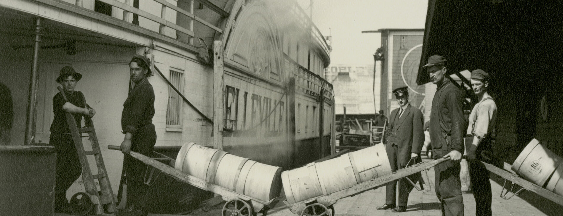 black and white image of people loading cheese onto a ship