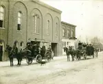 Firemen outside fire hall with horse-drawn vehicles.