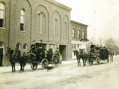 Firemen outside fire hall with horse-drawn vehicles.